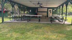 A covered picnic area with multiple tables and benches, surrounded by grass and trees. - RV-accessible cozy private campground with pool access near Lake Wallenpaupack (Hawley)