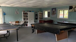 A room with a ping pong table, a foosball table, and a pool table. There are bookshelves and a clock on the wall. - RV-accessible cozy private campground with pool access near Lake Wallenpaupack (Hawley)