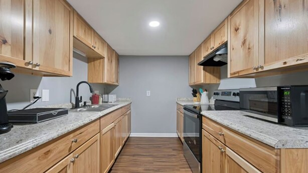 A modern kitchen with wooden cabinets, granite countertops, a stainless steel sink, a black range hood, and a microwave. - Spacious Backyard • Fireplace • Mins from Downtown (Glasgow)