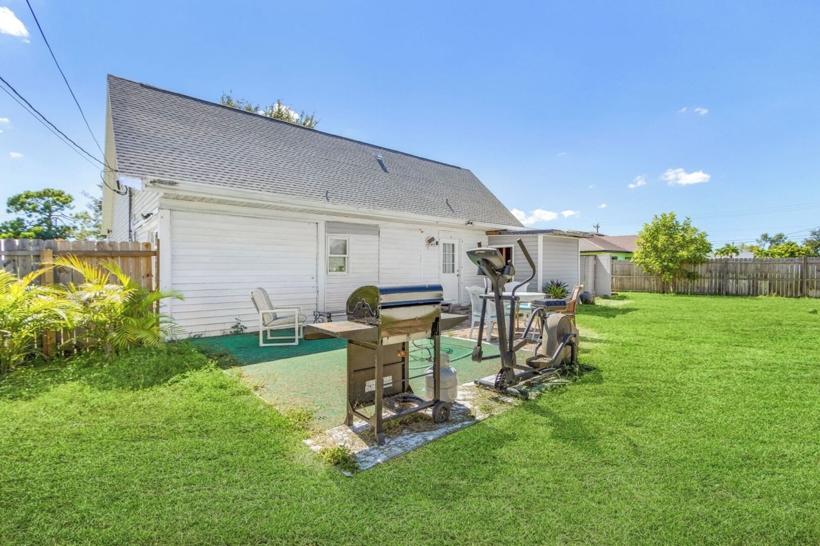 Un jardin à l’arrière d’une maison, aménagé avec une terrasse, du matériel d’exercice et un barbecue.
