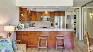 A modern kitchen with wooden cabinets, stainless steel appliances, and a central island with stools. - Beachfront • Pool + Hot Tub • Pickleball, Tennis (Lahaina)