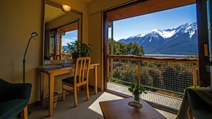 A room with a wooden desk, chair, and a large window offering a mountain view.