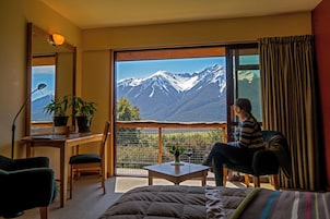 Una habitación con un amplio ventanal que ofrece vistas a la montaña, un escritorio con lámpara, una silla y una cama.