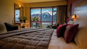 A hotel room with a large bed, a desk, and a chair. There is a view of mountains through the window.