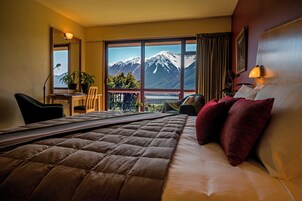 Habitación de hotel con una cama grande, un escritorio y una silla. Se ve una vista de montañas desde la ventana.