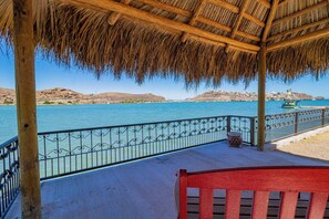 A wooden deck with a thatched roof overlooking a body of water, a metal railing, and a red bench. - Ocean front casa! Amazing views, jump into the water! Central location w/ wifi! (San Carlos Nuevo Guaymas)