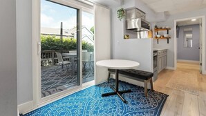 Una cocina moderna con horno integrado, microondas y campana extractora de acero inoxidable. Hay una zona de comedor con una mesa redonda y sillas, y una alfombra estampada azul en el suelo.