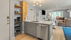Una cocina moderna con pared de ladrillo decorativa, una isla central y un área de comedor con sofá y mesa de centro.