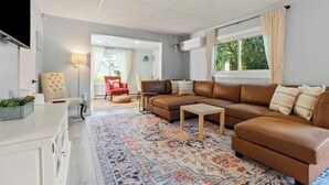 Una sala de estar moderna con un sofá de cuero marrón, un sillón rojo, una silla beige y una alfombra estampada.