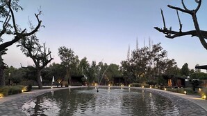 A tranquil outdoor area with a circular stone pond, surrounded by trees and illuminated by ambient lighting. - LUN Serena Lodge Chacras de Coria (Chacras de Coria)