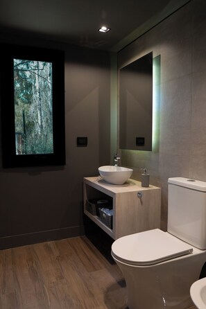 Et moderne badeværelse med en trækommode, en hvid vask og et toilet.