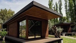 Ein modernes Haus mit Holzterrasse, großen Glasfenstern und einem Steinfundament.