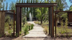 Ein Weg führt zu einem Gebäude mit einem Brunnen, umgeben von Bäumen und einem Metallgitter.