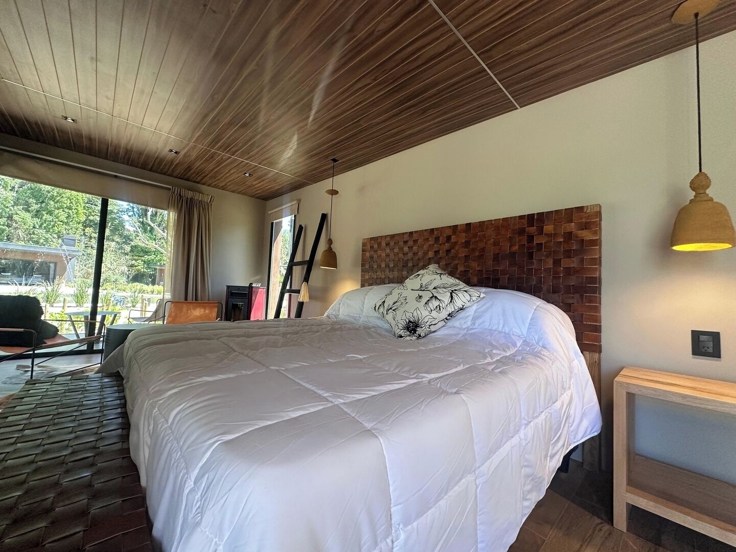 Ein großes Bett mit weißer Decke, einem Holz-Kopfteil und einer hängenden Pendelleuchte.