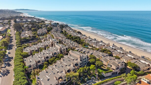 Luchtbeeld van een kustgebied met woonhuizen, een strand en een heldere lucht.