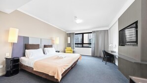A hotel room with a bed, a desk, a chair, a TV, and a window with curtains. - KozyGuru | Parramatta Studio Steps to Shops, Cafés (Parramatta)