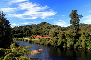 A serene lakeside view with a red-roofed building surrounded by lush greenery and a tall tree. - Wilderness Lodge Lake Moeraki (Lake Moeraki)