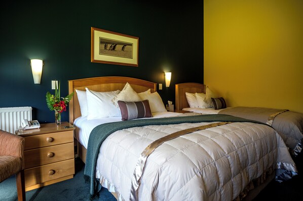 A hotel room with two beds, a nightstand with a lamp, a framed picture on the wall, and a vase with flowers. - Wilderness Lodge Lake Moeraki (Lake Moeraki)
