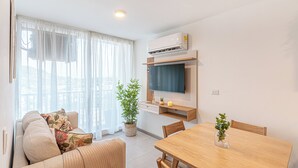 A modern living room with a sofa, a dining table, a TV mounted on the wall, and a potted plant. - Modern 3BR + Rooftop Pool & Jacuzzi (Cartagena de Indias)