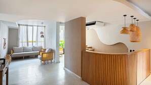 A modern reception area with a wooden reception desk, a seating area with a sofa and chairs, and a large window with curtains. - Modern 3BR + Rooftop Pool & Jacuzzi (Cartagena de Indias)