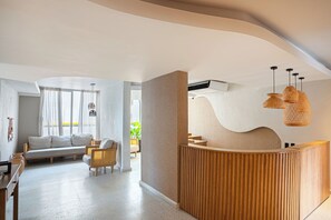 A modern reception area with a wooden reception desk, a seating area with a sofa and chairs, and a large window with curtains. - Modern 3BR + Rooftop Pool & Jacuzzi (Cartagena de Indias)