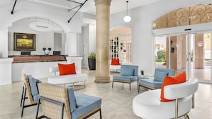 Un hall d’entrée avec un comptoir de réception, des fauteuils en osier, un canapé blanc et une grande colonne.