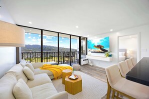Ein modernes Wohnzimmer mit Sofa, Couchtisch und Essbereich, mit großen Fenstern und Blick auf die Stadt.
