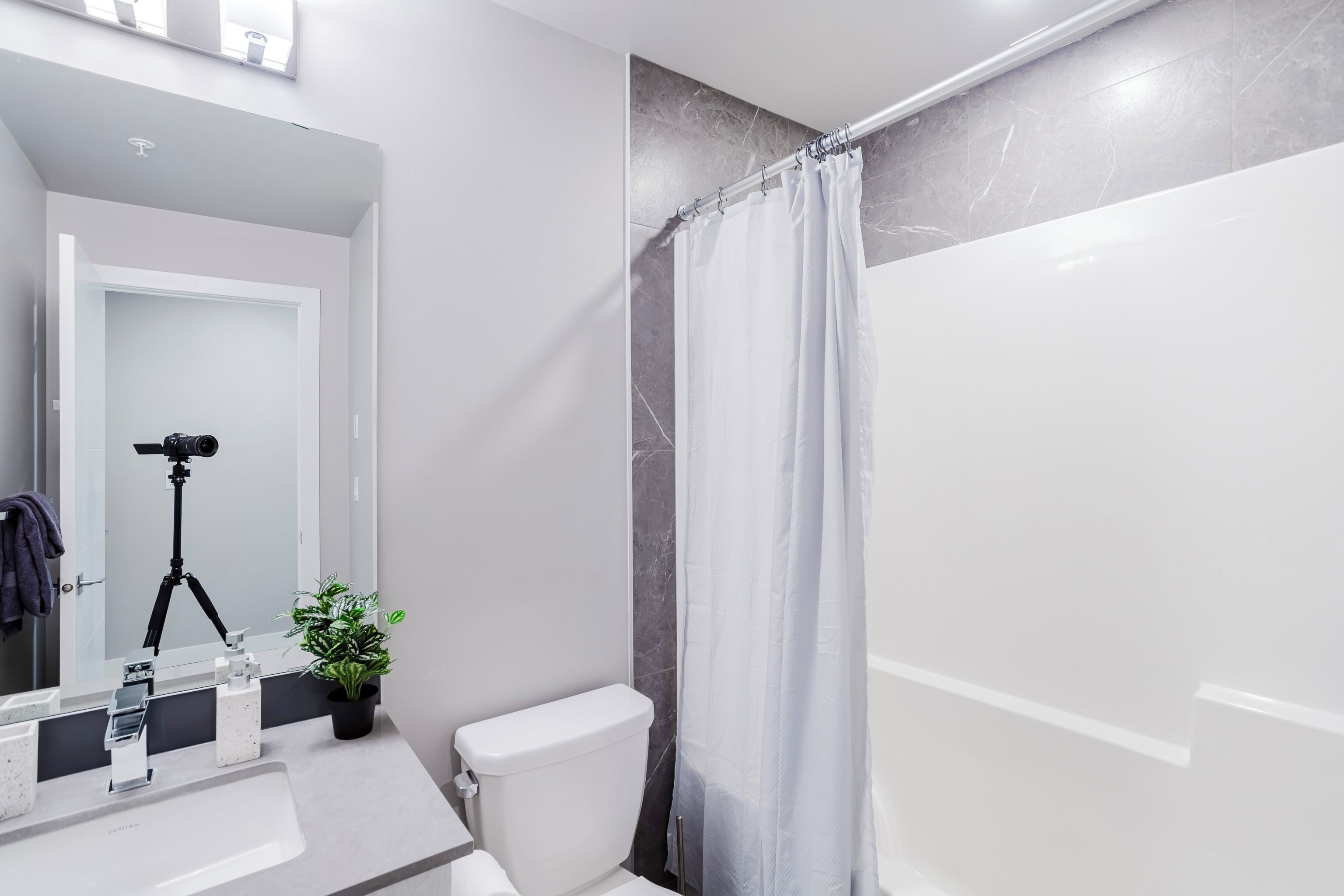 Un baño moderno con un lavamanos blanco, inodoro y ducha con cortina blanca.