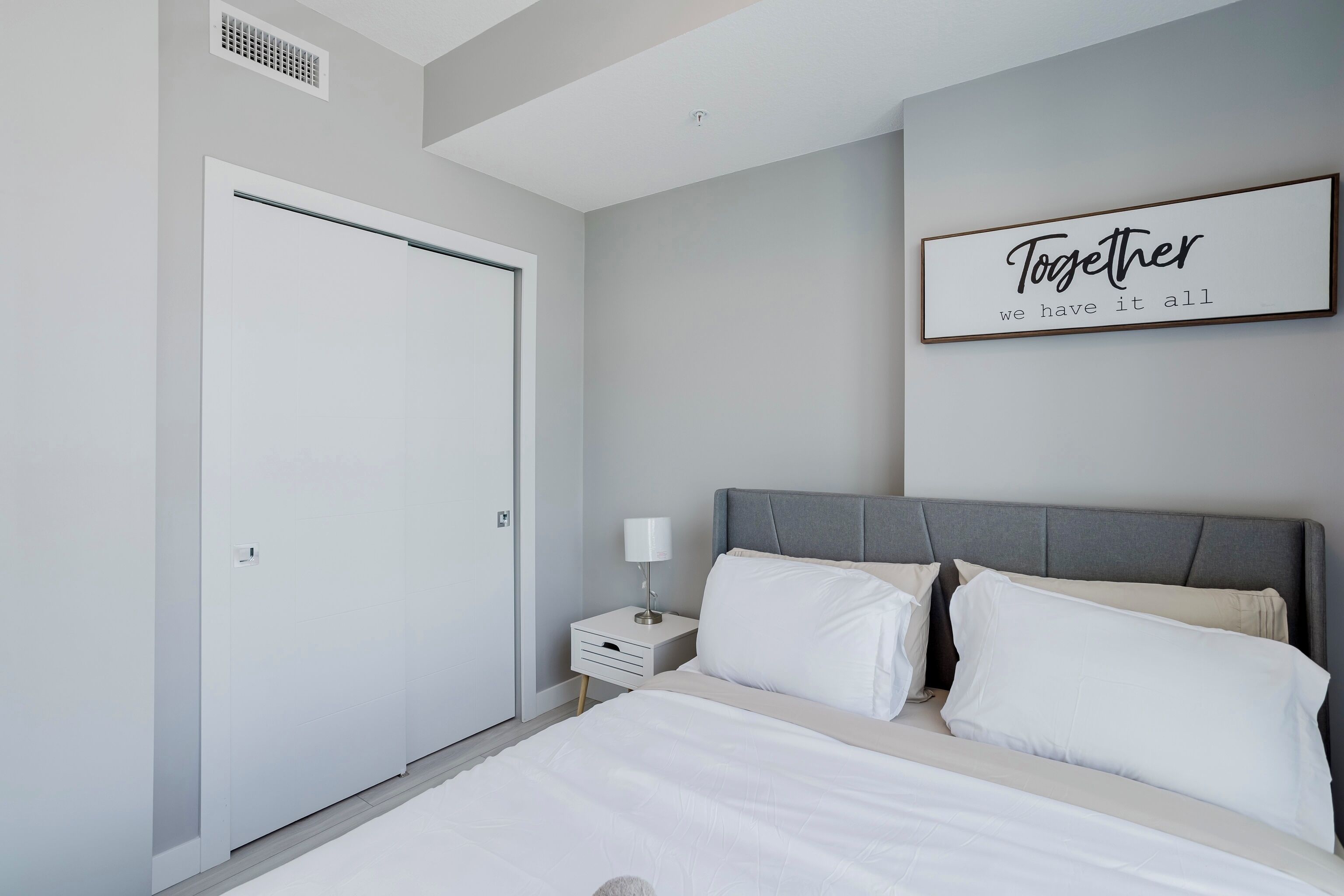 A bedroom with a bed, nightstand, and a framed sign on the wall.