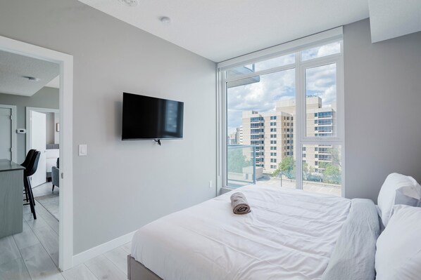 Ein modernes Hotelzimmer mit einem großen Bett, einem flachbildfernseher an der Wand und Blick auf die Stadt durch große Fenster.