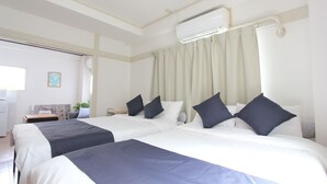 Hotelkamer met twee bedden, een plafondventilator, een airconditioning, een raam met gordijnen, en een tafeltje met een plant.