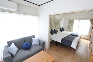 Une pièce avec un canapé gris, une table basse en bois, un lit avec deux oreillers et une fenêtre avec des rideaux.