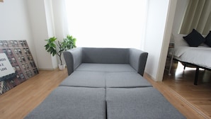 Een grijze modulaire bank in een moderne woonkamer met een houten vloer, een potplant en een lijst met een afbeelding aan de muur.