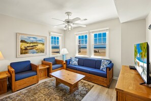 A living room with a sofa, chairs, a coffee table, and a TV. There are windows with beach views. - Dolphin: Dog-Friendly Buxton Beach Retreat (Buxton)