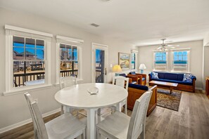 A spacious living room with a white round table, blue sofa, and a view of the beach through large windows. - Dolphin: Dog-Friendly Buxton Beach Retreat (Buxton)