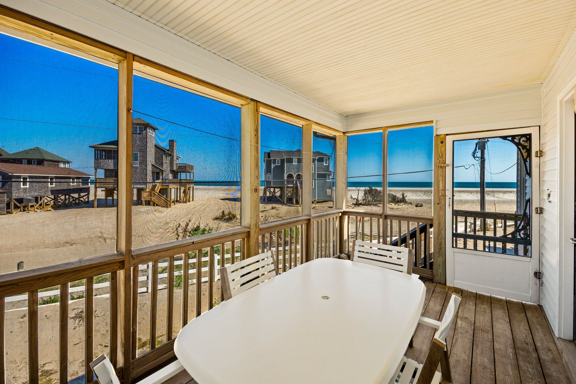 A beach house with a covered porch, a dining table, and a view of the beach and ocean.