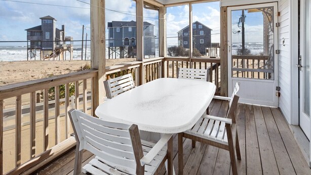 Ein überdachter Außenbereich mit Tisch und Stühlen mit Blick auf einen Strand und Häuser im Hintergrund.