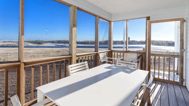 Un espace extérieur abrité, doté d’une table et de chaises, de grandes fenêtres et offrant une vue sur une plage et l’océan.