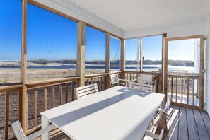 A covered outdoor area with a table and chairs, large windows, and a view of a beach and water. - Starfish: Dog-Friendly Buxton Townhome Near Beach (Buxton)