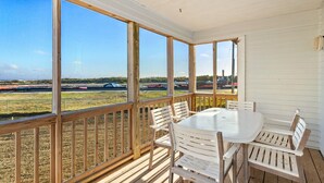 A covered outdoor patio with a table and chairs, overlooking a grassy field and an airport.