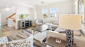 A modern living room with a sofa, a coffee table, a TV on a cabinet, a patterned armchair, and a ceiling fan.