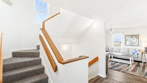 A staircase with wooden handrails leading to a landing, a living room with a sofa, a coffee table, and a rug.