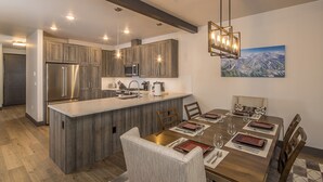 Una cocina moderna con armarios de madera, un refrigerador de acero inoxidable y un comedor con mesa y sillas de madera.