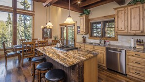 Una cucina con un'isola grande, sgabelli da bar in legno e vista sulla foresta attraverso ampie finestre.
