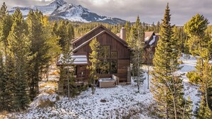 Una baita di legno circondata da terreno e alberi innevati, con una montagna sullo sfondo.