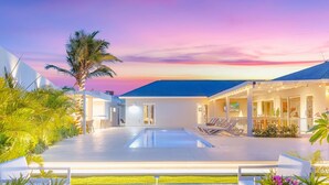 Un resort moderno con piscina, sillas de descanso y vistas al atardecer.