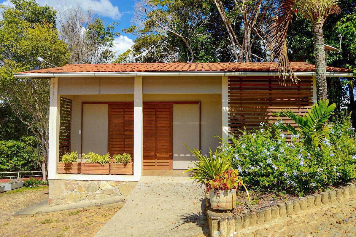 A small building with a tiled roof, wooden doors, and a stone foundation. There are potted plants in front and a stone wall to the right.