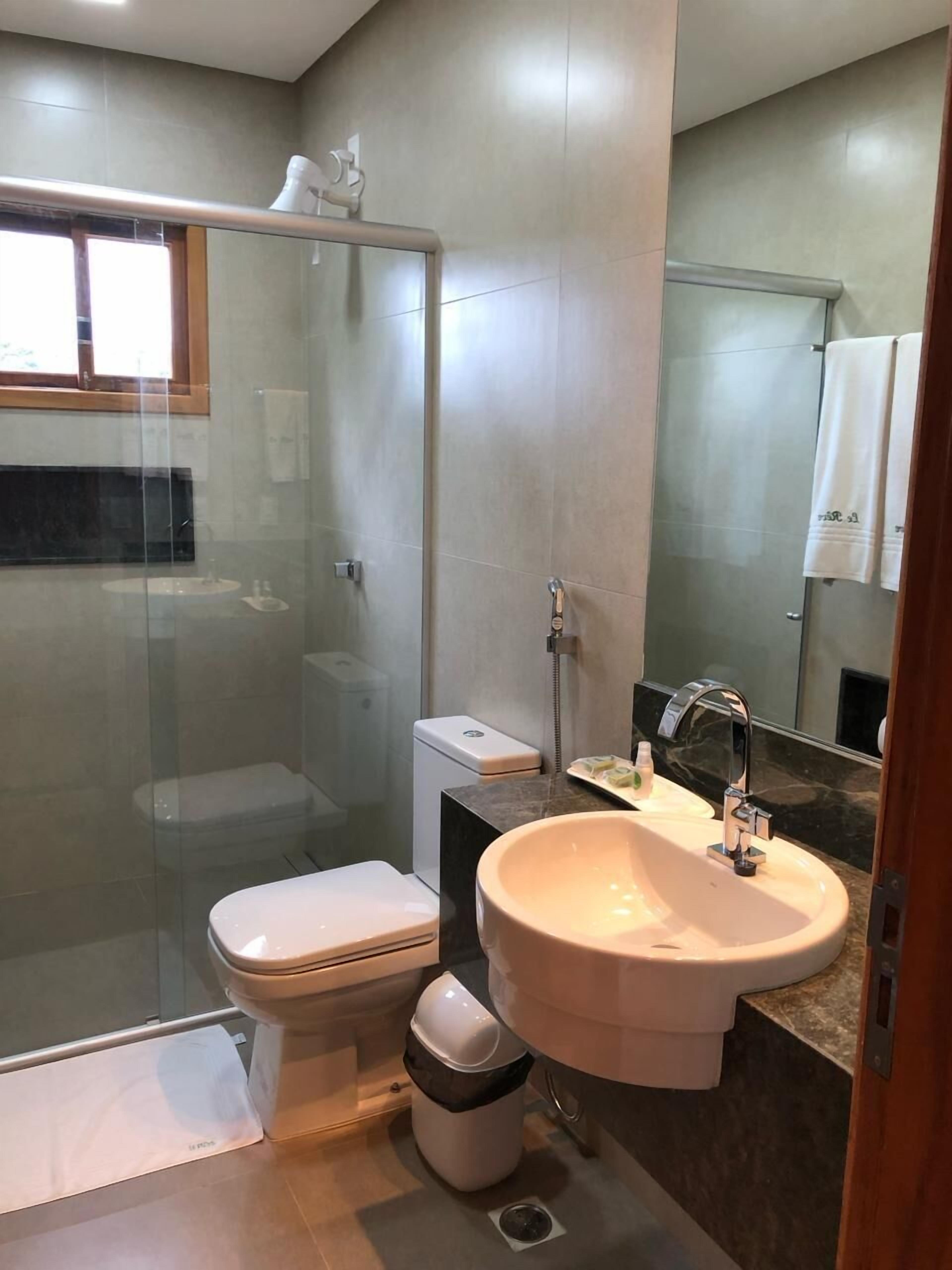 Un baño moderno con ducha envuelta en vidrio, inodoro, lavabo y espejo.