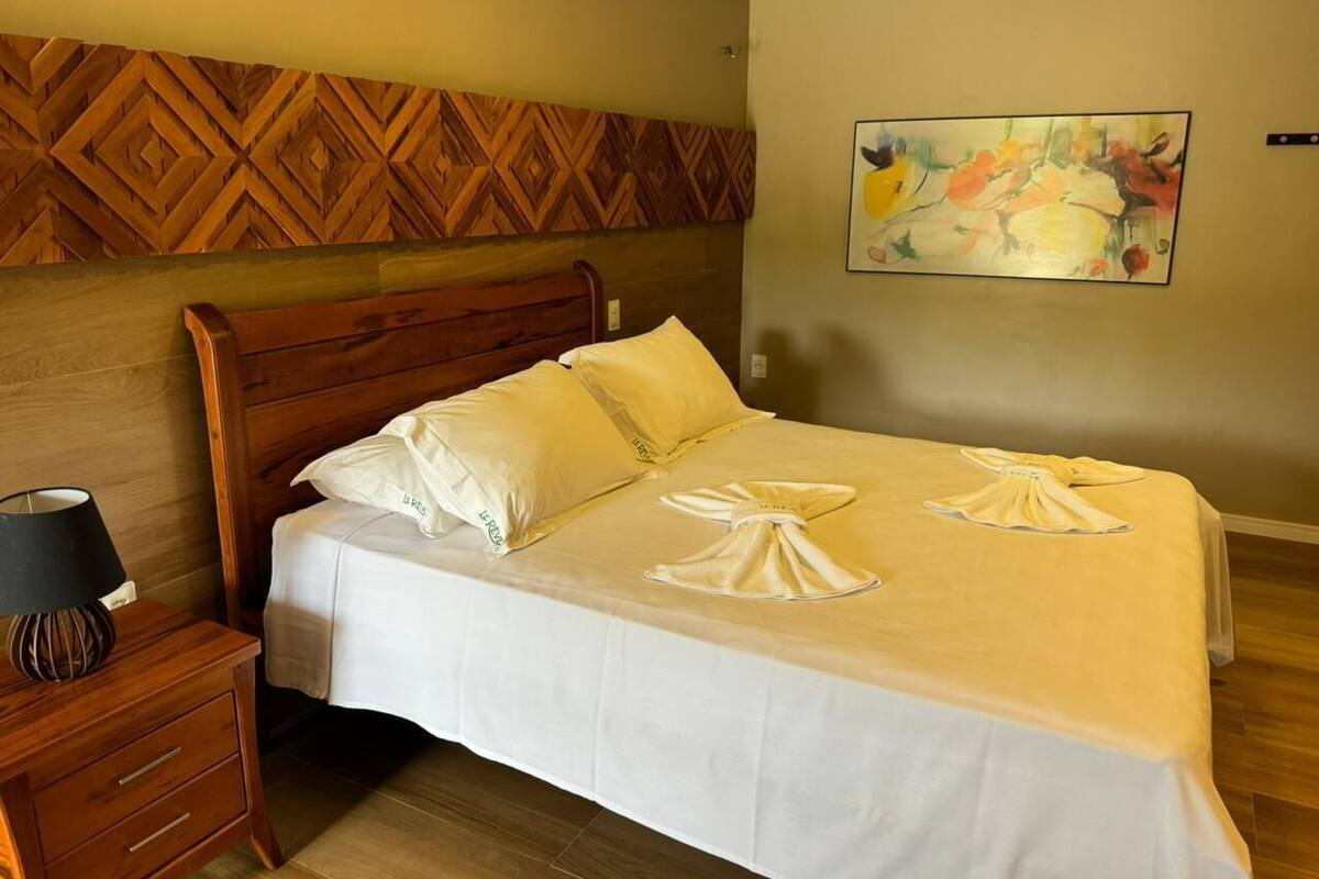 A neatly made bed with pillows, a bedside table with a lamp, and a wooden headboard.