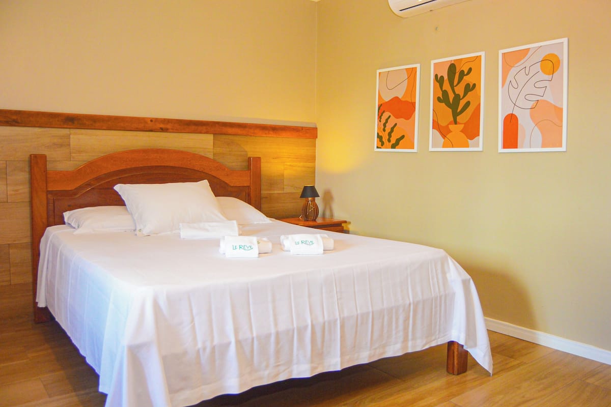 A neatly made bed with white linens, a wooden headboard, and a nightstand with a lamp and a vase.